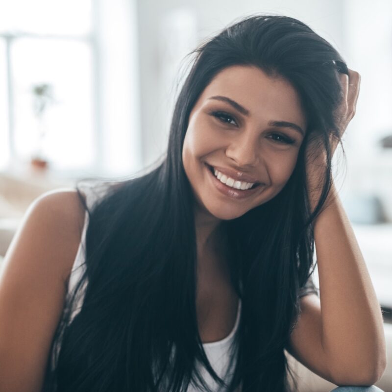Perfect smile. Portrait of beautiful young woman looking at camera and smiling while sitting on the couch at home